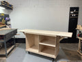 Light wood portable cart with shelves and an extended tabletop in a workshop.