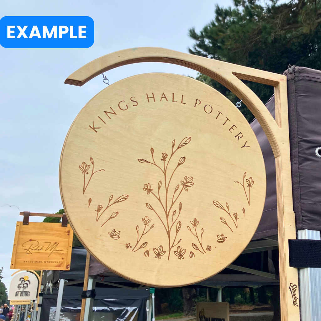 Wooden sign for 'Kings Hall Pottery' with floral design against a blue sky in a Dublin market