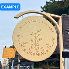 Wooden sign for 'Kings Hall Pottery' with floral design against a blue sky in a Dublin market