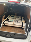 Flat-packed wooden portable coffee cart components with logos, secured in a white van.
