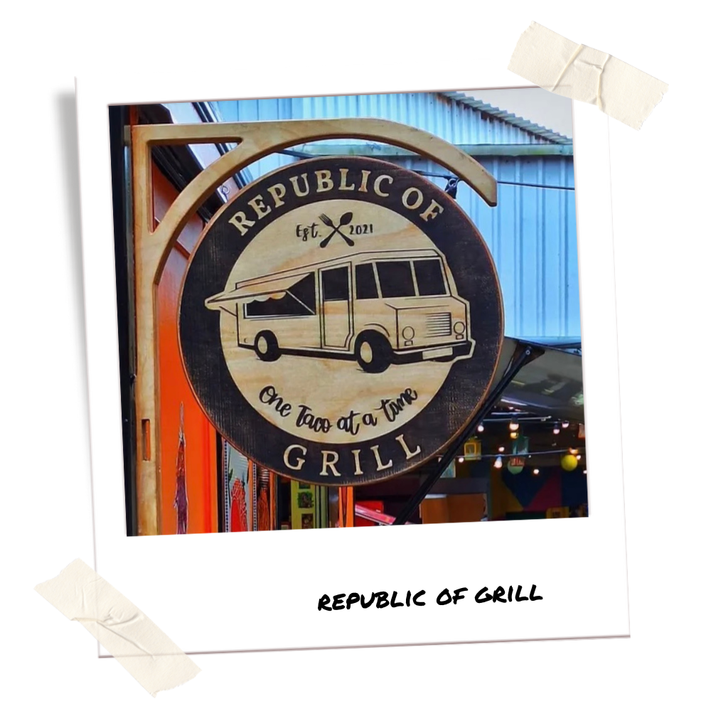 Wooden sign with 'Republic of Grill' branding in front of a colorful building.